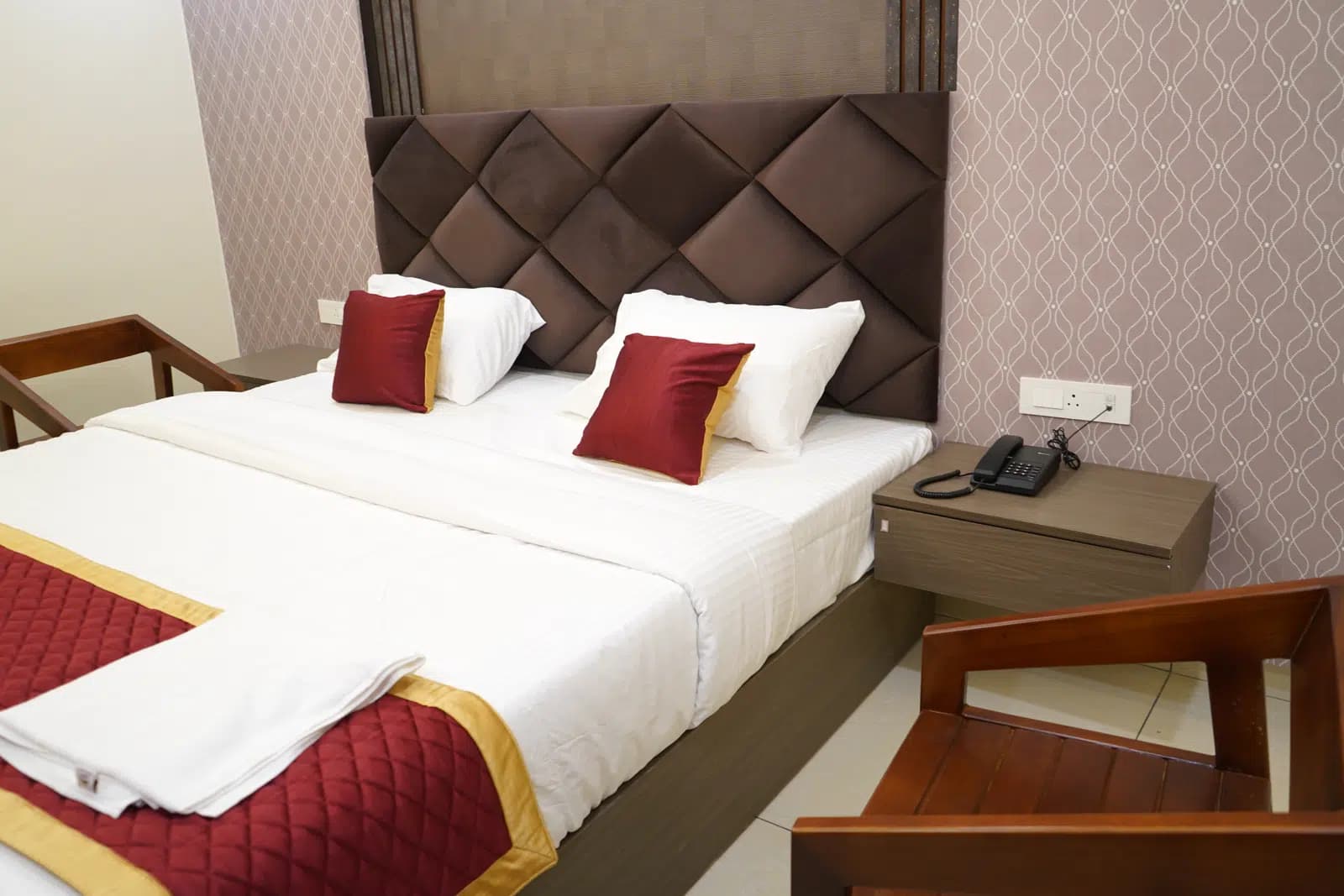 Deluxe room bed with a bedside telephone and wooden armchair